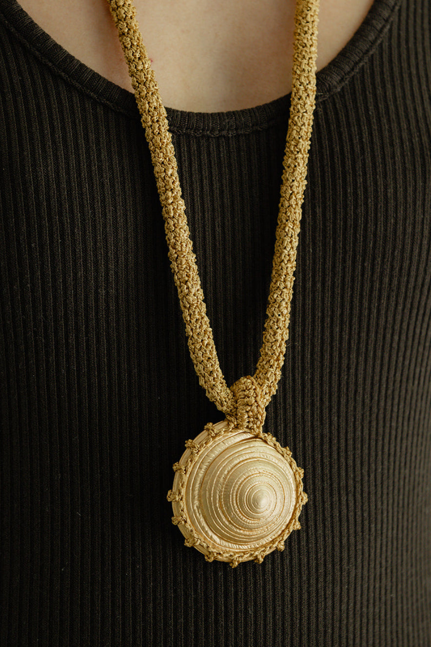 Gold crochet necklace with a circular seashell pendant worn by a person in a black top.