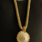 Gold crochet necklace with a circular seashell pendant worn by a person in a black top.