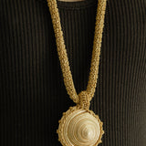 Gold crochet necklace with a circular seashell pendant worn by a person in a black top.